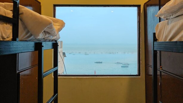 A bunk bed room with a window view of the sea and boats. - NS BACKPACKERS HOSTEL (VARANASI)