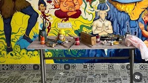 A room with a mural of deities, a small table with art supplies, and a patterned floor. - NS BACKPACKERS HOSTEL (VARANASI)