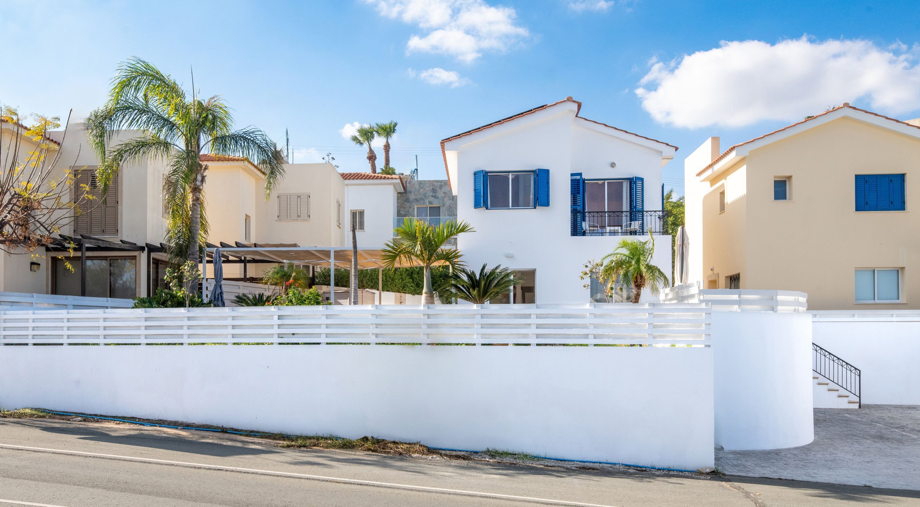 A coastal residential area with white houses, palm trees, and a clear sky.