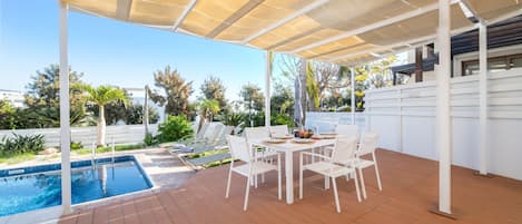 Zona exterior coberta amb piscina, cadires blanques i una taula amb plats i gots.