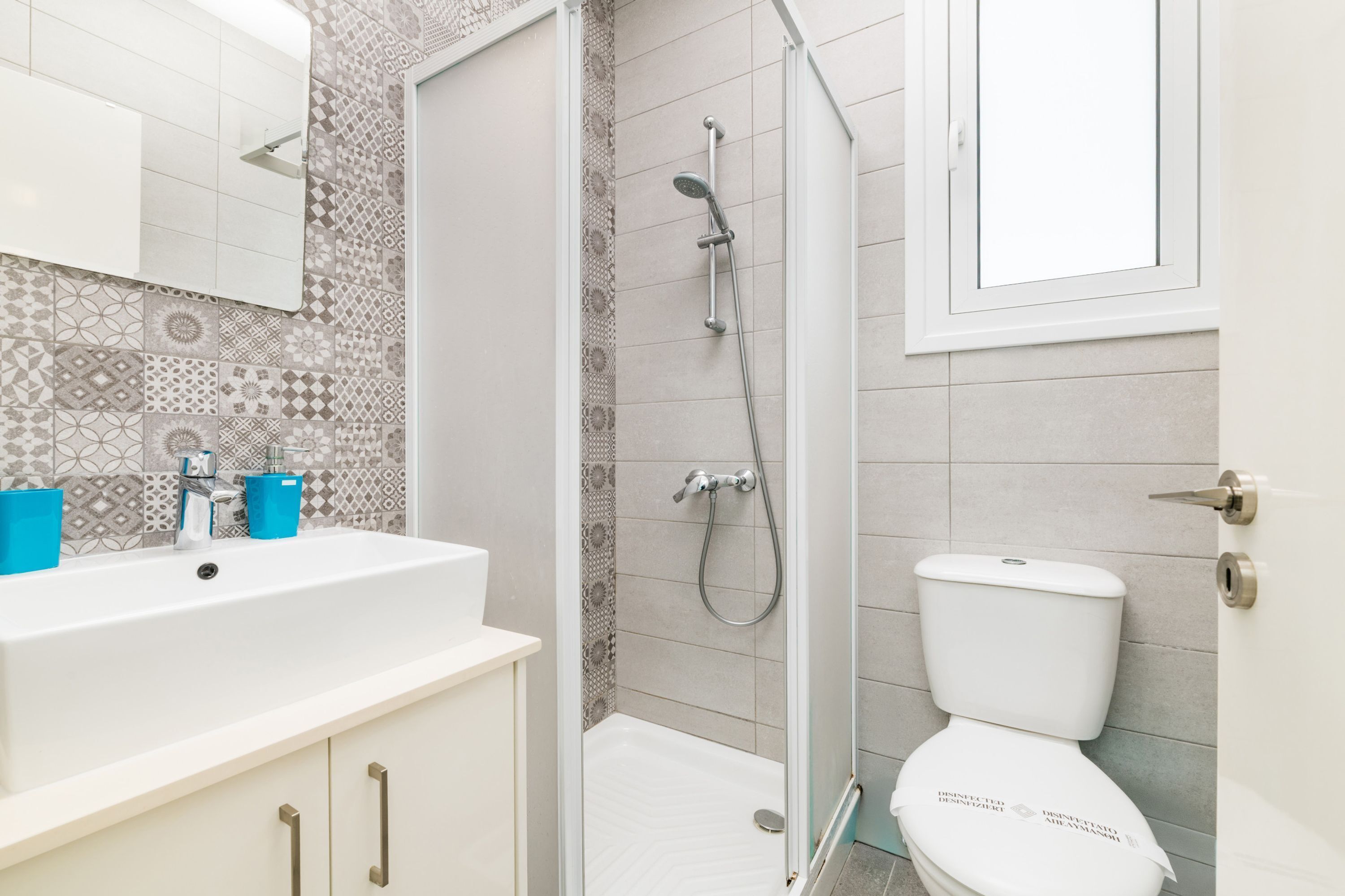 A modern bathroom with a white sink, blue soap dispensers, a glass shower enclosure, and a white toilet.