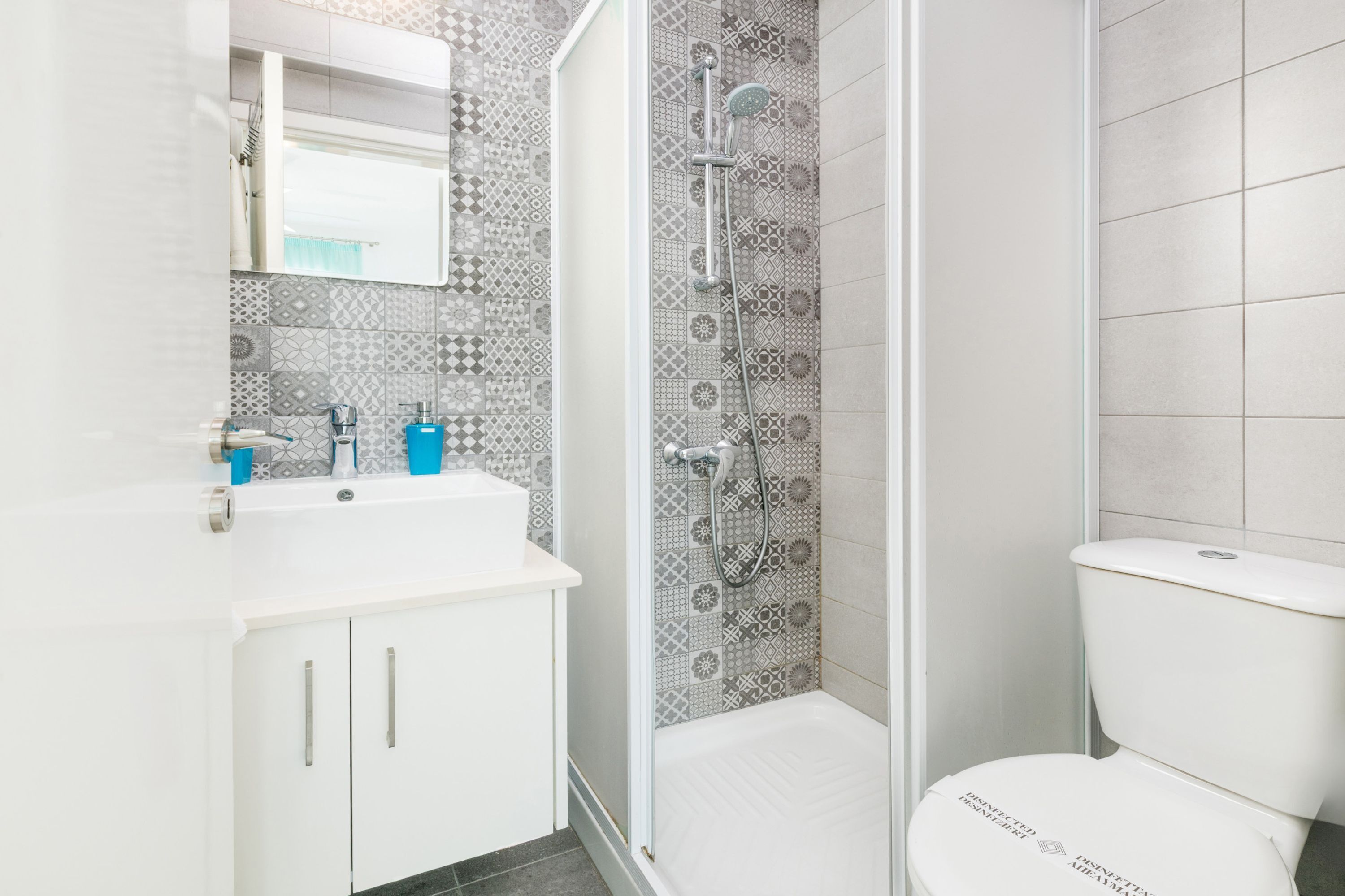 A bathroom with a white sink, a mirror, a shower with a patterned wall, and a toilet.