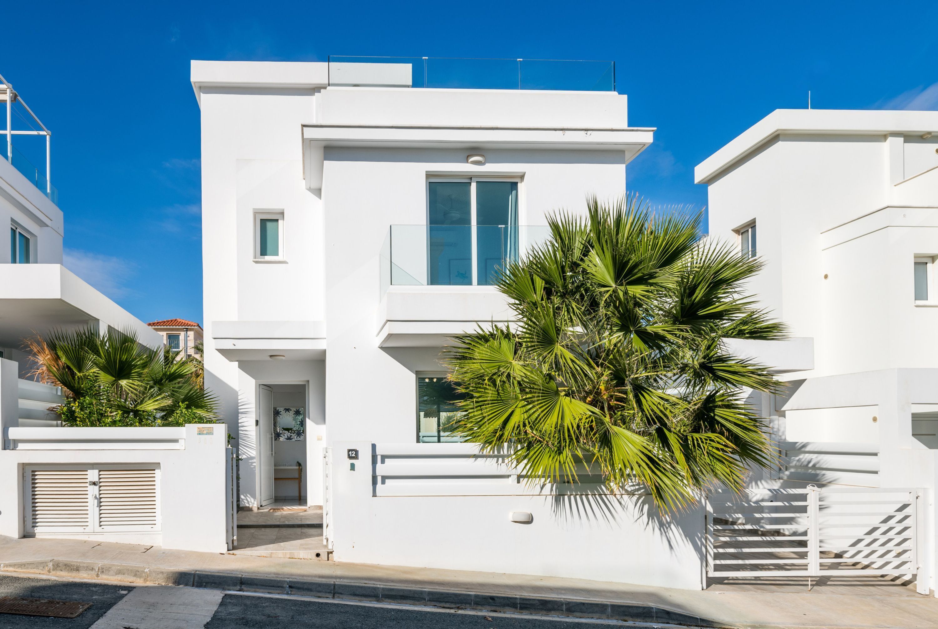Un edificio moderno blanco con balcones y una palmera en primer plano.