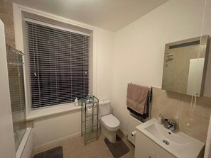 A bathroom with a toilet, a glass shelf with toiletries, a towel rack, and a mirror. - Cozy 1-bedroom Apartment Near Margate Seafront (Margate)