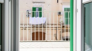 A balcony with a metal railing, a view of a building with green shutters, and a white cloth hanging on the railing. - [Urban Home 29] Modern Apartment - Molfetta (Molfetta)
