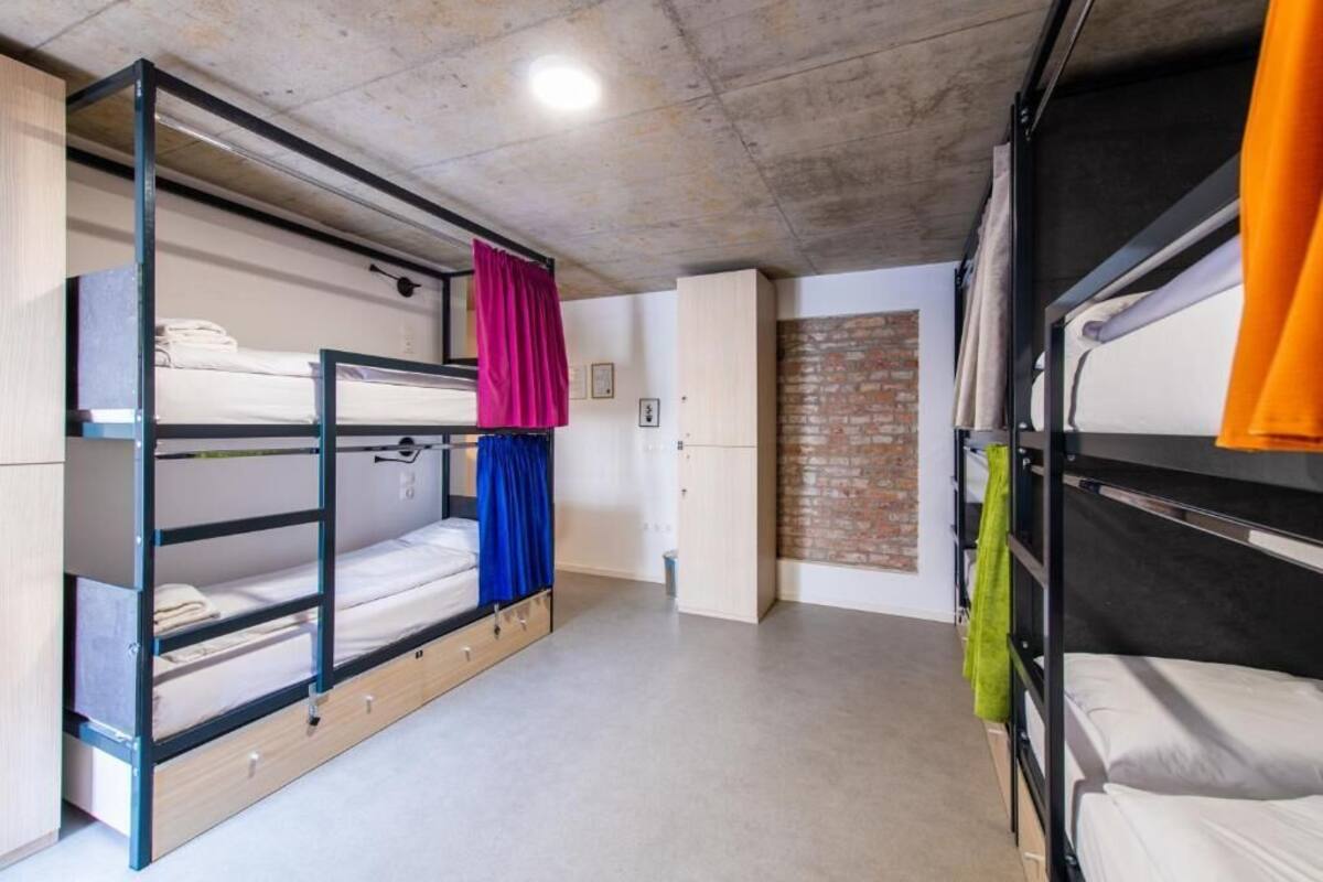 A bunk bed room with a concrete ceiling, a brick wall, and a door leading to another room.