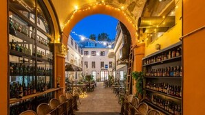 An indoor corridor with wooden chairs and tables, shelves with bottles, and a sign for a "HOTEL" in the background. - City Rooms OS (Osijek)