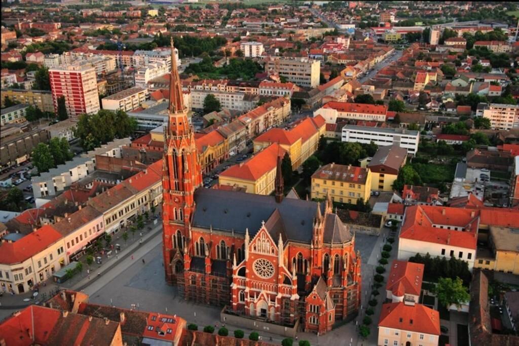 An aerial view of a city with a prominent red-brick church featuring a tall tower and a large circular window.