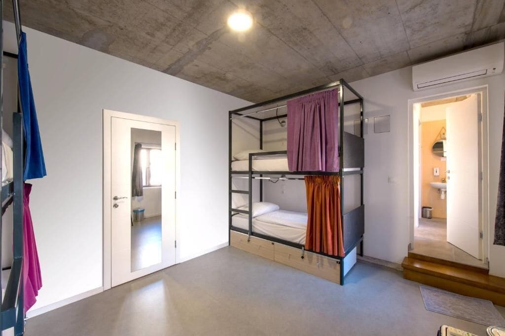 A bunk bed room with a white door, a bathroom visible through an open door, and a concrete ceiling.