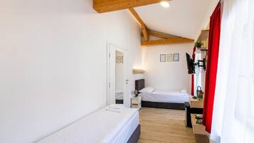 Une chambre avec deux lits, des poutres en bois, un bureau et un rideau rouge.