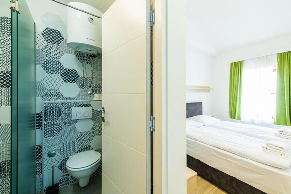 A hotel room with a bed, a bathroom with a toilet and shower, and a green curtain.