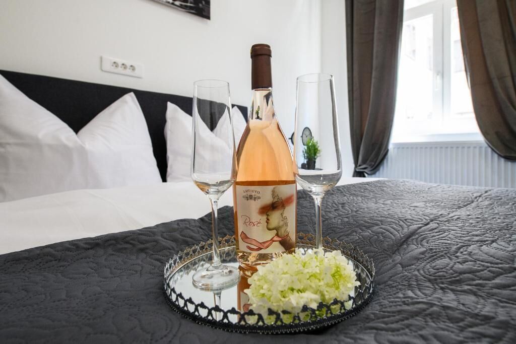 A bed with a black headboard, a bottle of rosé wine, two wine glasses, and a tray with white flowers.