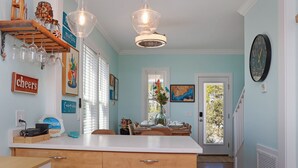 A kitchen with a white countertop, wooden cabinets, a hanging light fixture, and a dining area with a table set for two. - ☀️ Pet Friendly - Private Pool - Screened Deck - Indian Shores Cottage ☀️ (Indian Pass)