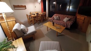 A living room with a sofa, a dining table with chairs, a coffee table, and a TV cabinet. - Le 20cts - T3 with balcony and terrace (Bagnères-de-Bigorre)