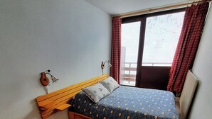 A bedroom with a bed, wooden headboard, a nightstand, a window with curtains, and a radiator. - Le 20cts - T3 with balcony and terrace (Bagnères-de-Bigorre)