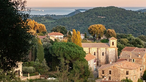 Un village perché sur une colline, avec des bâtiments en pierre, une église et une vue sur la mer.