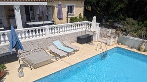 Une piscine avec des chaises longues et des parasols, un mur de pierre et un bâtiment doté d’un balcon en arrière-plan.