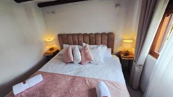 A neatly made bed with a headboard, two bedside lamps, and a window with curtains.