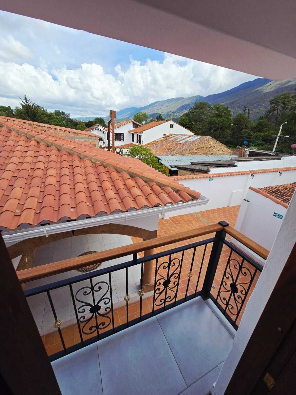 A balcony with a tiled roof, a metal railing, and a view of houses and mountains.