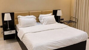 Een hotelkamer met een groot bed, twee nachtkastjes met lampen, een hoofdbord en een raam met gordijnen.
