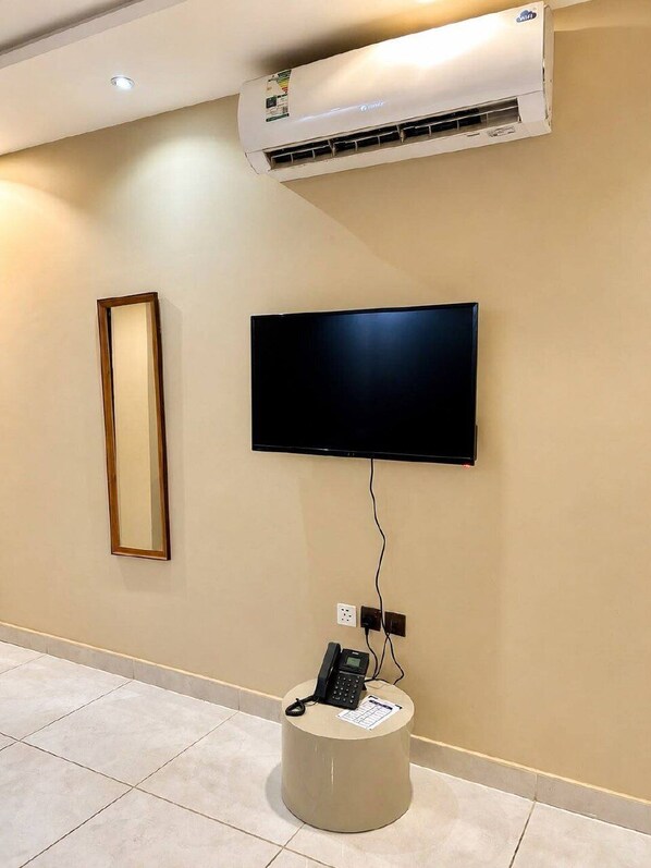 A room with a mounted flat-screen TV, a telephone on a small table, and an air conditioning unit on the wall. - Mdmak Suites (Riyadh)