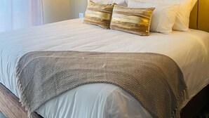 A neatly made bed with a patterned throw blanket, a beige headboard, and a bedside lamp. - Petalite Villa Maun (Maun)