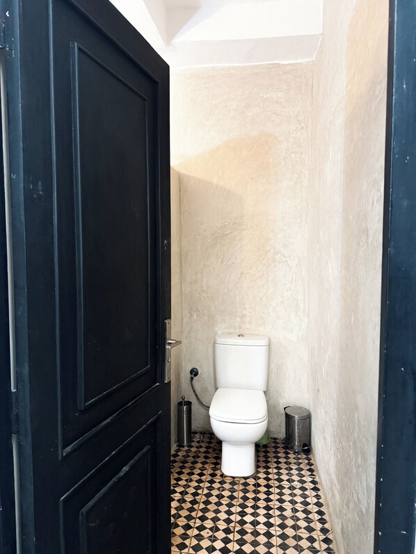 A small, narrow bathroom with a black door, a white toilet, and a tiled floor. - dar al bahar Taghazout -beachfront (Taghazout)
