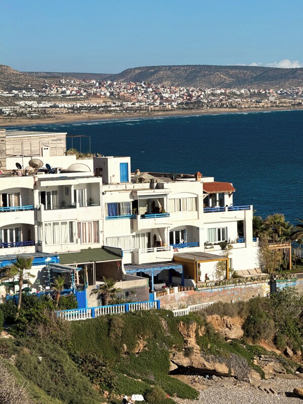 A coastal residential area with modern white buildings, a clear view of the sea, and a hilly landscape in the background. - dar al bahar Taghazout -beachfront (Taghazout)