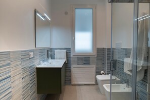 A modern bathroom with a glass shower enclosure, a built-in sink, and a toilet. - Marusu Apartments First Floor (Terrasini)