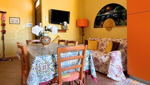 Un comedor con una mesa dispuesta para cuatro, un sofá, un televisor montado en la pared y un cuadro sobre el sofá.