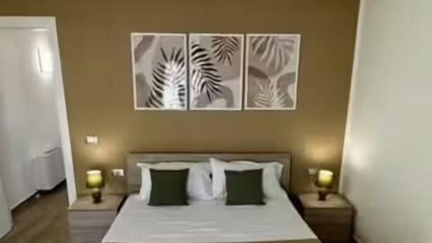Un letto rifatto con cura, con una testiera marrone, due comodini con lampade e decorazioni alle pareti sopra il letto.