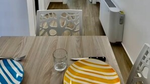 Un couloir étroit qui se termine par un coin repas, avec une table où sont disposés deux assiettes et un verre, une chaise et un radiateur fixé au mur.