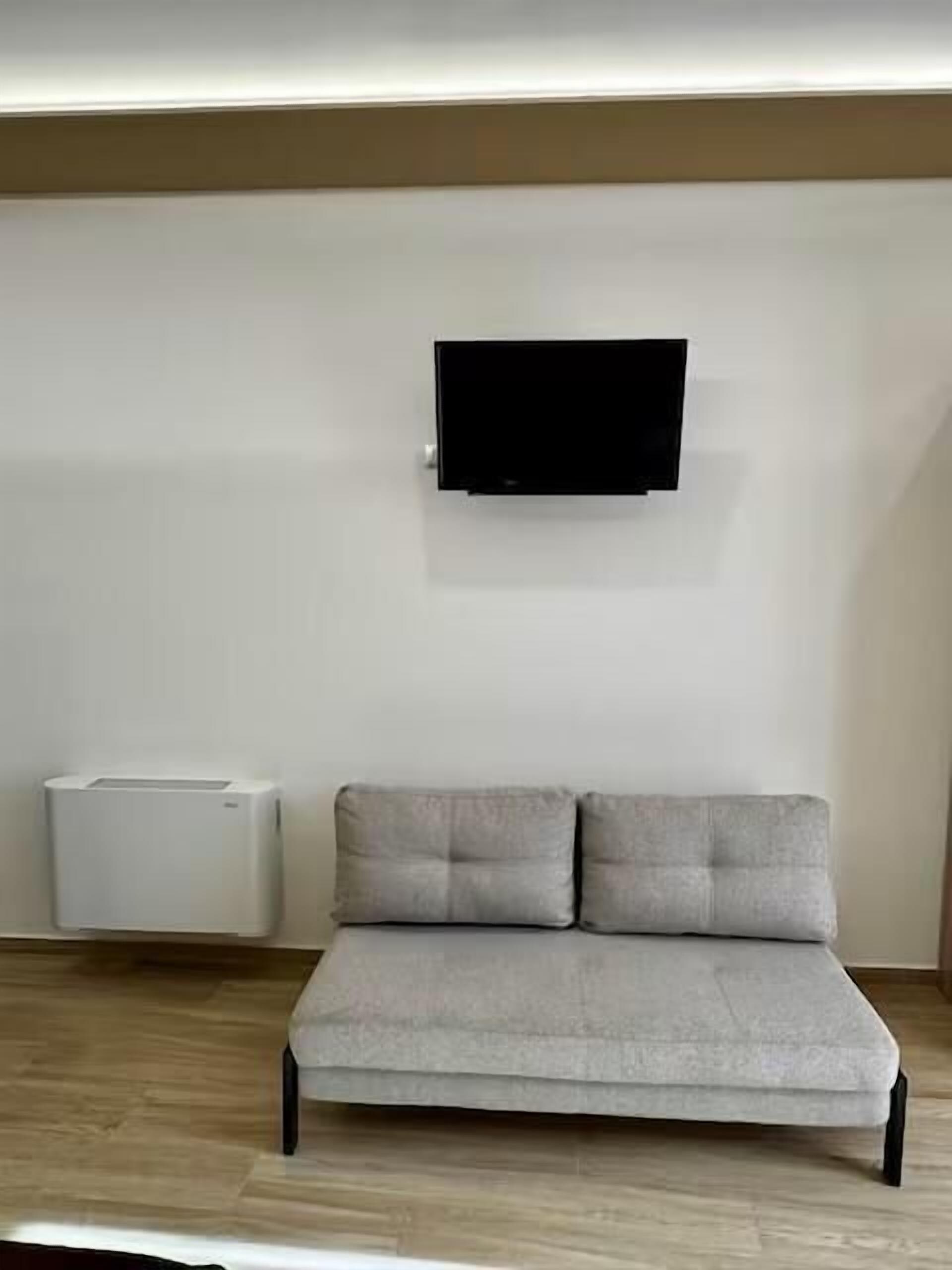 A modern living room with a flat-screen TV mounted on the wall, a grey sofa, and a white air conditioning unit.
