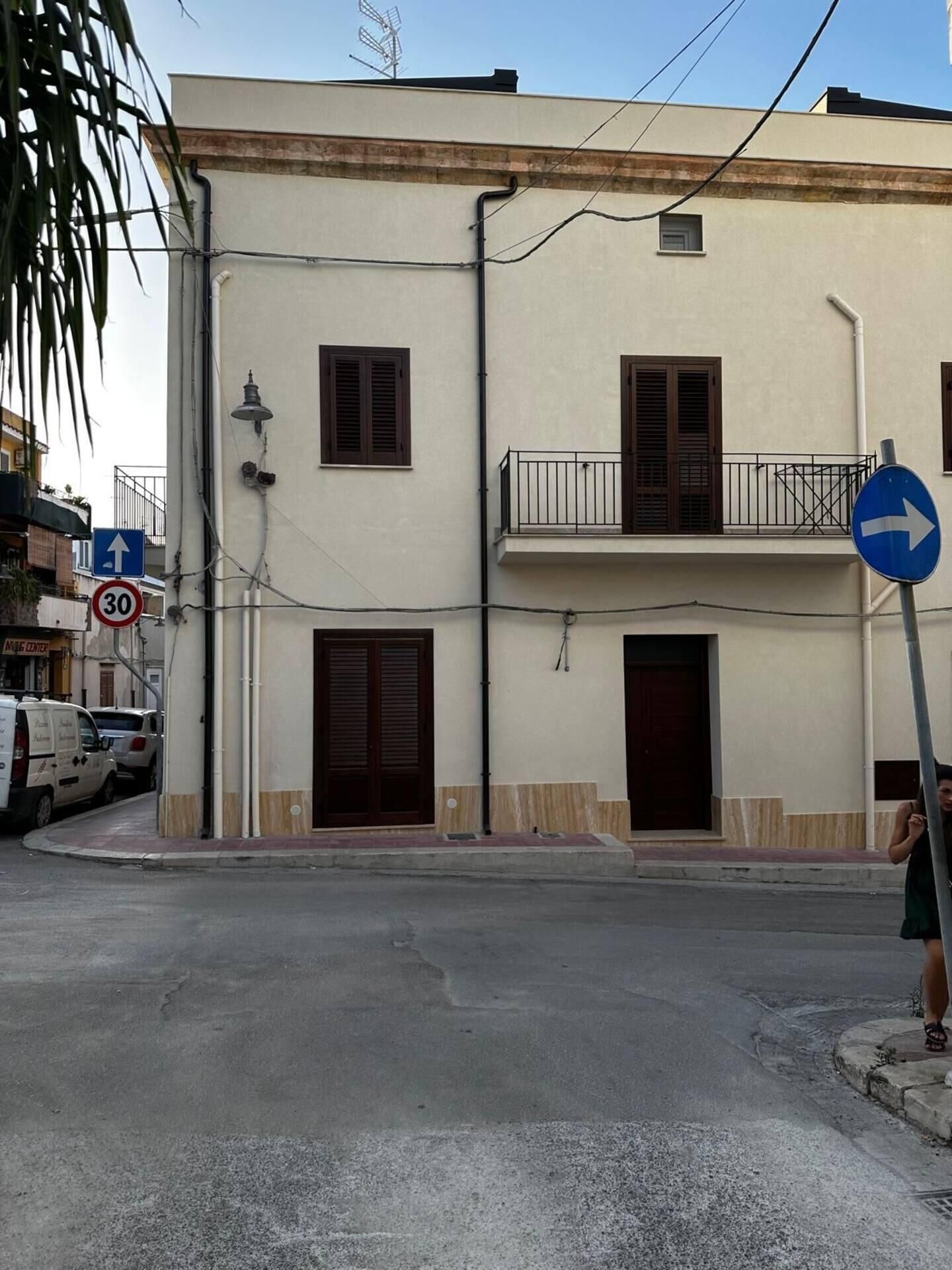 A building with a white facade, multiple windows, and a balcony. There is a blue directional sign on the right.