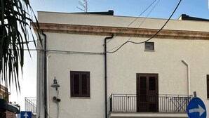 Ein Gebäude mit weißer Fassade, mehreren Fenstern und einem Balkon. Rechts ist ein blaues Hinweisschild zu sehen.