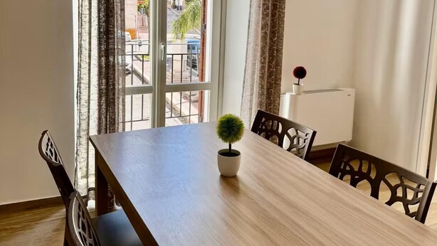 A dining area with a wooden table, chairs, a potted plant, and a view through a glass door to the outside. - Apartment with Balcony (TERRASINI)