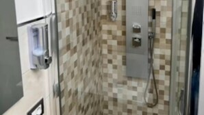 Un espace douche clos par des parois de verre, avec des murs carrelés à motifs à carreaux et une pomme de douche visible.