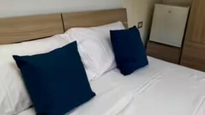 Un lit avec des oreillers blancs et bleu foncé, une tête de lit en bois et un mur blanc.