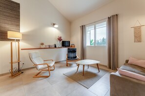 Una sala de estar moderna con un sofá, una butaca, una mesita, un televisor y una ventana con cortinas.
