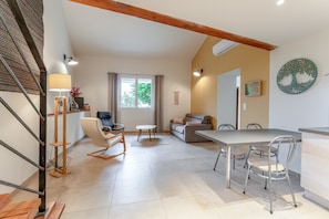 A spacious living area with a dining table, sofa, and a staircase with wooden beams. - Gîte le Jolia – Cottage with Pool (Nyons)