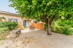 A stone building with a wooden fence, a gravel patio, and a tree providing shade.