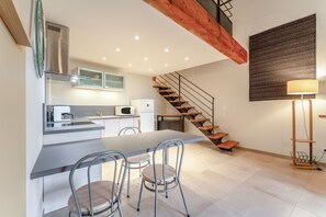 A modern kitchen with a dining area, a staircase, and a wall-mounted lamp.