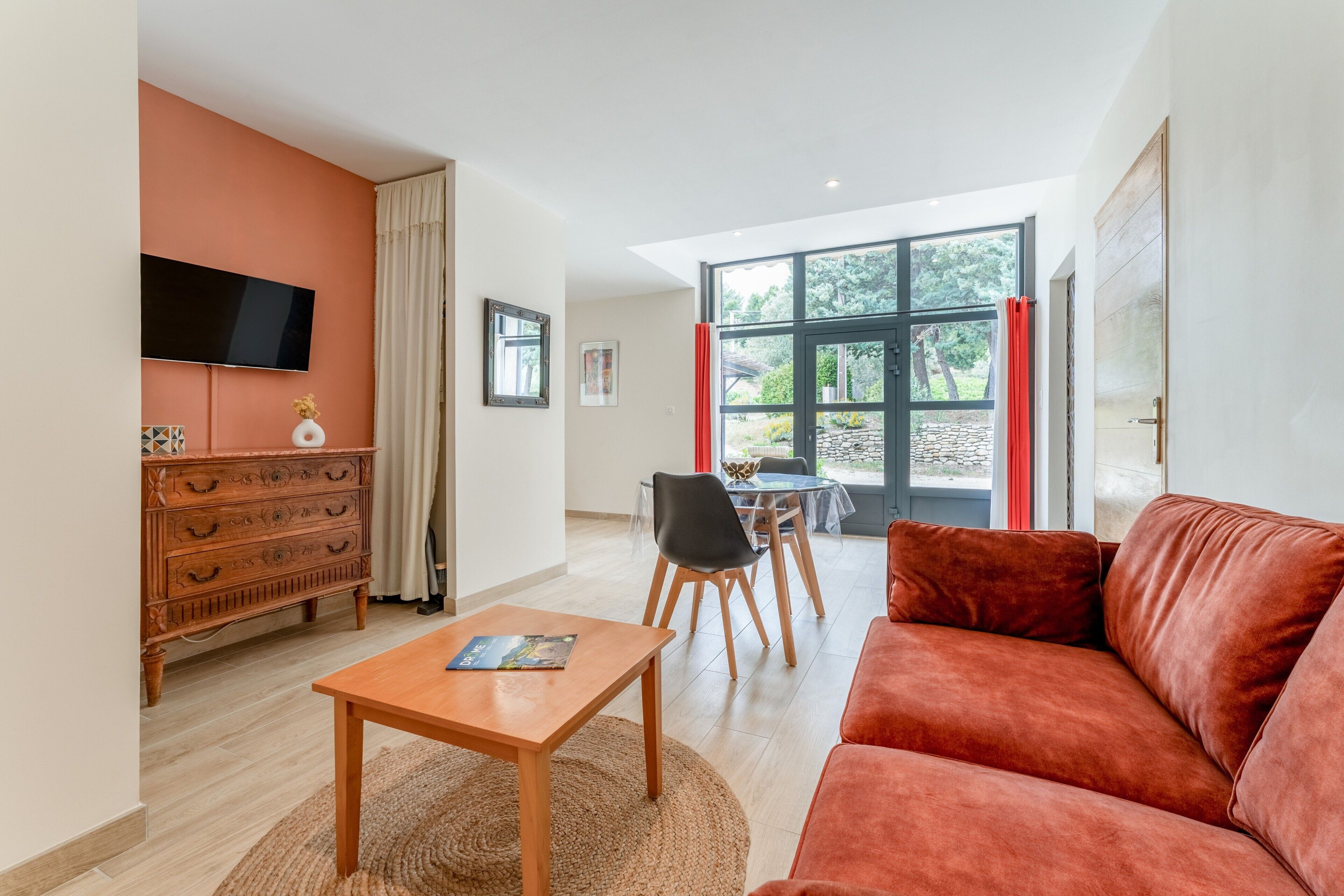 Sala de estar com sofá, televisão fixada na parede, mesa de madeira e área de jantar com cadeiras e mesa.