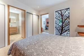 Een slaapkamer met een bed, een kledingkast, een spiegel en een decoratief paneel met een boom.