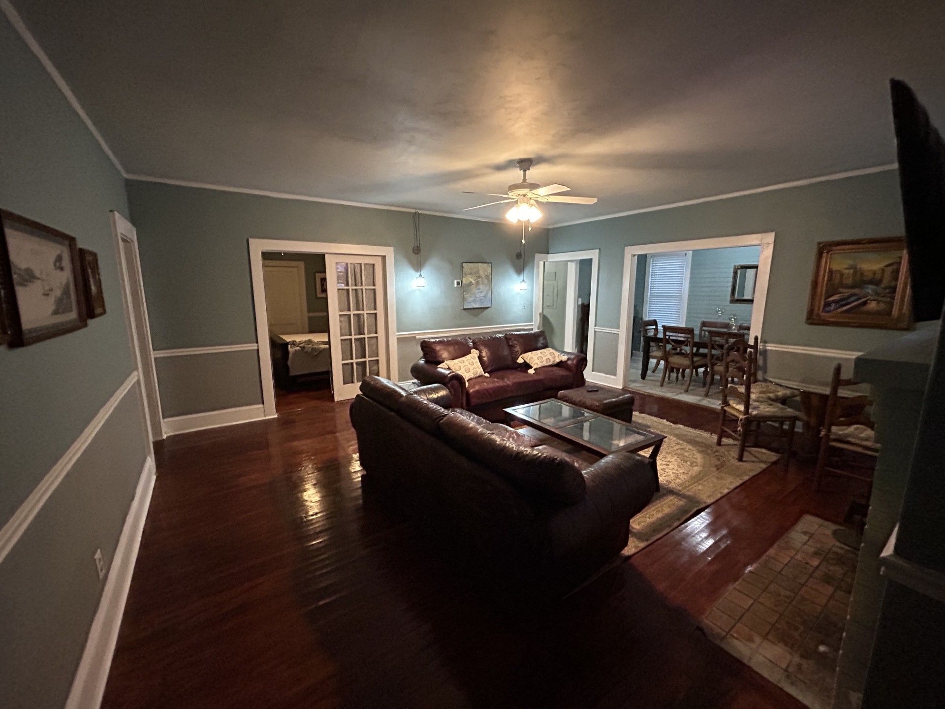 A spacious living room with a dark brown leather sofa, a glass coffee table, and a ceiling fan.