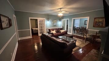 A spacious living room with a dark brown leather sofa, a glass coffee table, and a ceiling fan.