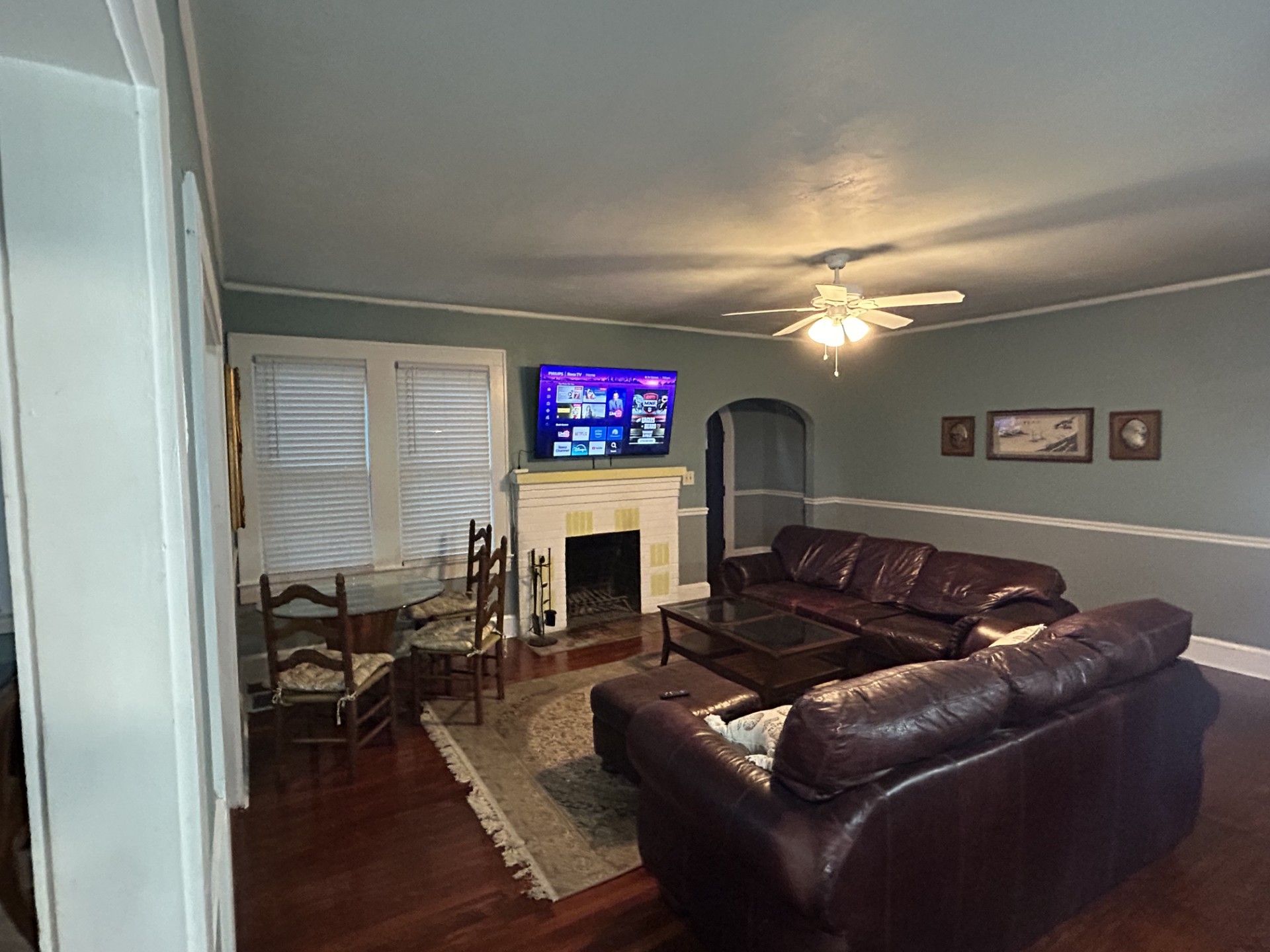 A living room with a fireplace, leather sofa, television, and ceiling fan.