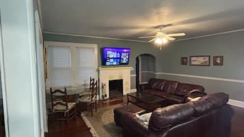 A living room with a fireplace, leather sofa, television, and ceiling fan.