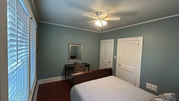 A bedroom with a bed, a desk, a chair, a ceiling fan, and two doors.