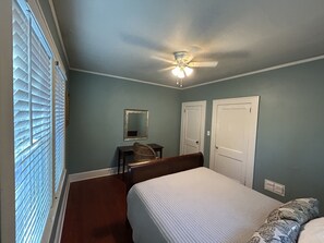 A bedroom with a bed, a desk, a chair, a ceiling fan, and two doors. - Southern Comfort (Tallahassee)